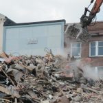 a bulldozer digging through a pile of rubble in front of a building