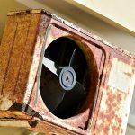 a rusted metal fan mounted to the side of a building